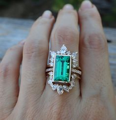 a woman's hand holding an emerald and diamond ring