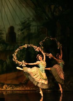 two ballerinas are performing on stage with their arms in the air and holding flowers