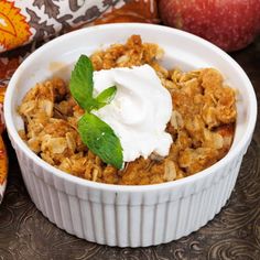 a bowl filled with granola and topped with whipped cream next to an apple on the side