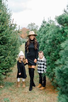 a woman and two children walking through a christmas tree farm