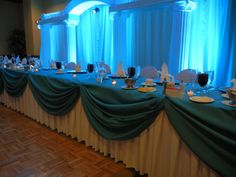 a banquet table set up with place settings and blue drapes on the windowsill