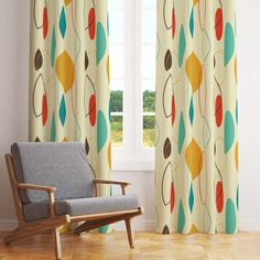 a chair sitting in front of a window next to a curtain with leaves on it