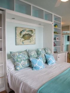 a bed with blue and white pillows in a bedroom next to a book shelf filled with books