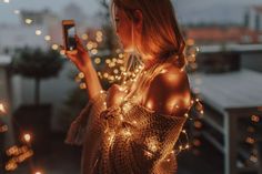 a woman standing on a roof looking at her cell phone with lights all around her