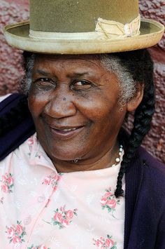 an older woman wearing a green hat with braids on her hair and smiling at the camera