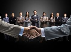 two men shaking hands in front of a group of business people with their arms crossed