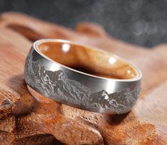 a wedding band with mountains etched on it sitting on a piece of wood in front of some rocks