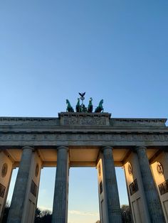 an arch with statues on top in front of a blue sky and some trees around it