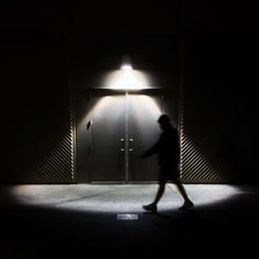 a person walking in front of an open door at night with a light on it