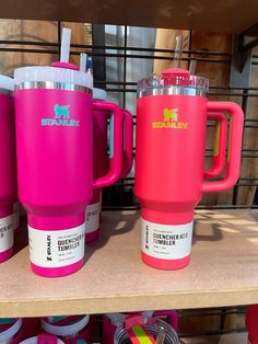 three pink coffee mugs sitting on top of a wooden shelf next to other cups