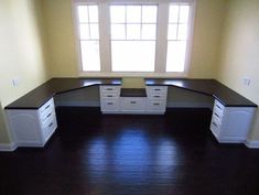 an empty room with white cabinets and black counter tops in the corner, along with dark wood flooring