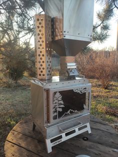 a stove sitting on top of a wooden table in the middle of a field next to trees