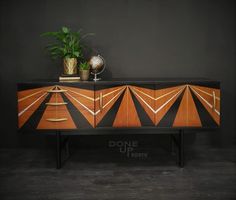 an art deco sideboard with orange and black designs on the front, two plants in vases on top