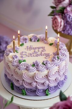 a birthday cake with purple frosting and three lit candles on top, surrounded by flowers