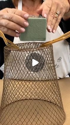 a woman holding a cell phone in front of a wire basket on top of a table