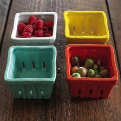 four plastic containers with raspberries and grapes in them on a wooden table top