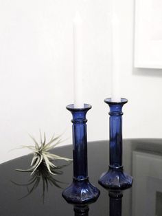 two blue candles sitting on top of a table next to a small airplant