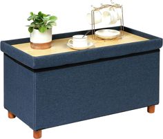 a blue ottoman with two cups on it and a plant in the middle is shown