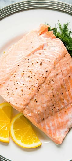 a piece of salmon sitting on top of a white plate next to lemon wedges