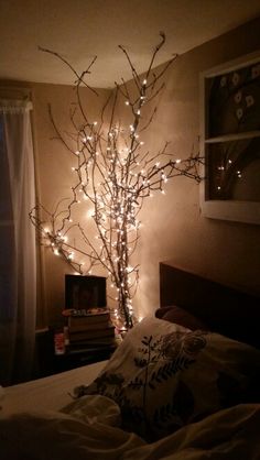 there is a tree with lights in the corner of this room and it looks like someones bedroom