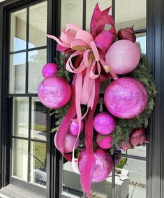 a wreath with pink ornaments hanging on the front door