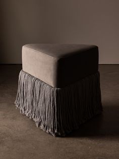 a foot stool with fringes on the top and bottom, against a dark background