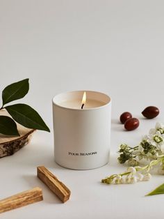 a white candle sitting on top of a table next to some dried flowers and olives