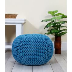 a blue crocheted poufce sits on the floor next to a potted plant