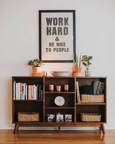 a wooden shelf with books and plants on it in front of a framed work hard poster