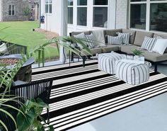 a black and white striped rug on the outside of a house with couches, coffee table and potted plants