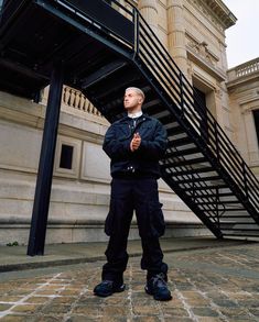 a man standing in front of a building with a stair case next to him and looking up