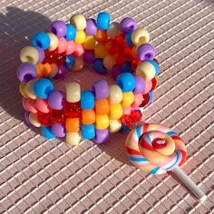 Kandi bracelet with colorful beads and matching lollipop charm. Bracelet has a base of 28 beads.  Bead Colors: Yellow, white, blue, red, purple, orange, pink, lollipop charm Measurements: 17.5 - 23 cm l, 3.5 cm w The length measurement is of the circumference of the bracelet. The first number is the inner circumference, the second is the outer circumference. All bracelets are stretchy and size my vary slightly due to the elastic stretch. When putting on and taking off your cuff bracelet make sure to slide/push wiggle the bracelet onto your hand, as opposed to pulling and stretching the bracelet onto your wrist. Too much stretching and pulling can rip and break the elastic. Handmade Sweet Style Multicolor Beaded Bracelets, Sweet Multicolor Beaded Bracelets, Sweet Multicolor Round Bead Bracelets, Pony Bead Jewelry, Bracelets Kandi, Pony Bead Animals, Pink Lollipop, Safety Pin Crafts, Pony Bead Bracelets