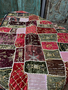 a patchwork table cloth with various colors and designs on it, sitting in front of an old wooden door