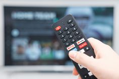 a hand holding a remote control in front of a television screen with the tv on