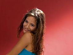 a woman with long hair posing for a photo in front of a red background wearing a blue tank top