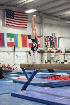 a person on a balance beam in an indoor gymnastics gym with flags and people watching