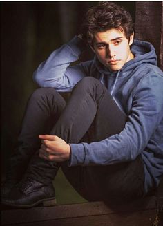 a young man sitting on top of a wooden bench wearing a blue hoodie and black pants