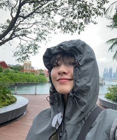 a woman wearing a rain jacket and carrying a backpack in front of a body of water