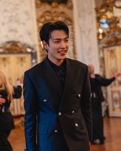 a young man in a suit and tie standing on a wooden floor with other people behind him