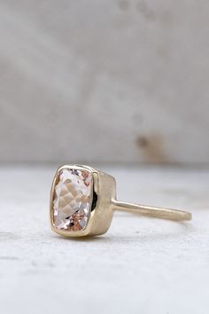 a gold ring with a pink diamond in it sitting on a white surface, next to a wall