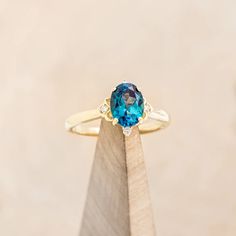 an oval blue topaz ring sits atop a wooden stand with a diamond on it