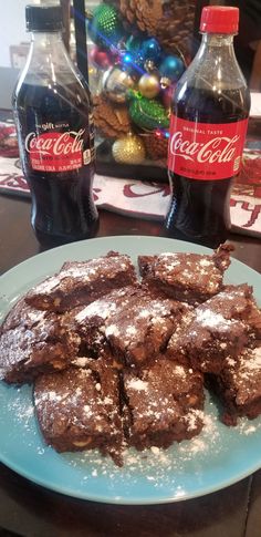 chocolate brownies with powdered sugar and coca - cola bottles on the table next to it