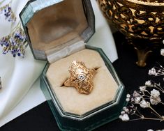 an ornate gold ring sits in a glass box on a table next to some flowers