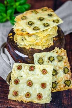 three pieces of food sitting on top of a wooden table next to a plate with cheese and olives