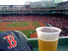 a cup of beer sitting on top of a table in front of a baseball field