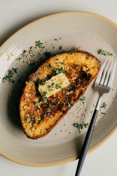 a piece of bread with cheese and herbs on it next to a knife and fork