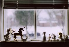 a window sill filled with figurines of horses and unicorns on top of it