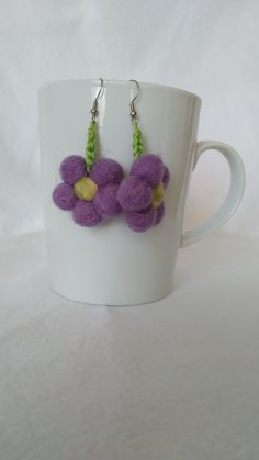 two purple flowers are hanging from the handle of a coffee cup with silver earwires