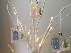 a white christmas tree decorated with small houses and trees are hanging from the branches, which have lights on them