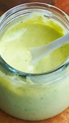 a jar filled with green liquid sitting on top of a wooden table next to a spoon